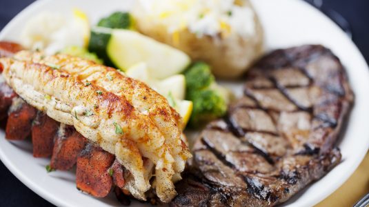 Plate of steak, lobster, mashed potatoes, and vegetables for dinner