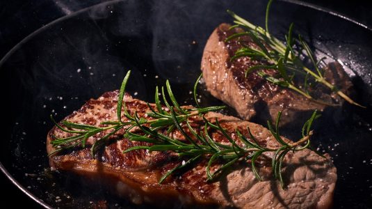 Steak cooking on pan with rosemary on the top